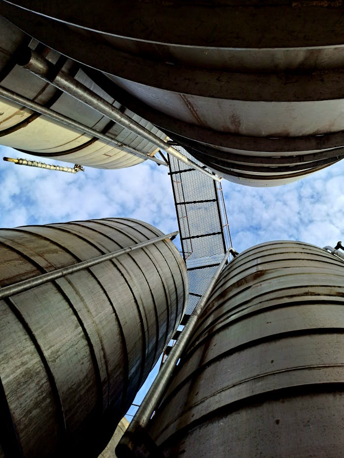 our-stories Low angle view of industrial storage tanks and a sky bridge against a blue sky.